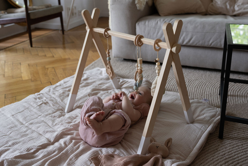 Baby spielt auf einer Decke unter dem Holzspielbogen