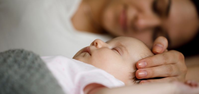 Baby schläft und Mama streichelt mit der Hand über den Kopf des Babys
