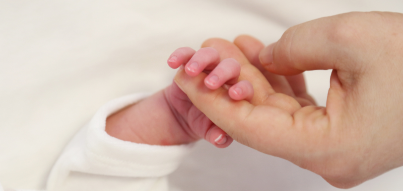 Hand eines Neugeborenen umfasst einen Finger seiner Mama. Die Anzeichen einer bevorstehenden Geburt sind so individuell wie das Leben selbst.